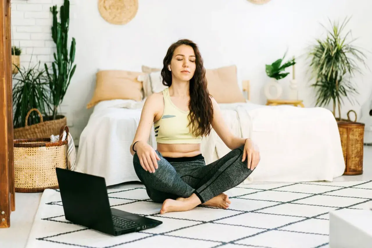Mujer meditando en posición de loto, aprendiendo técnicas de relajación con un portátil.