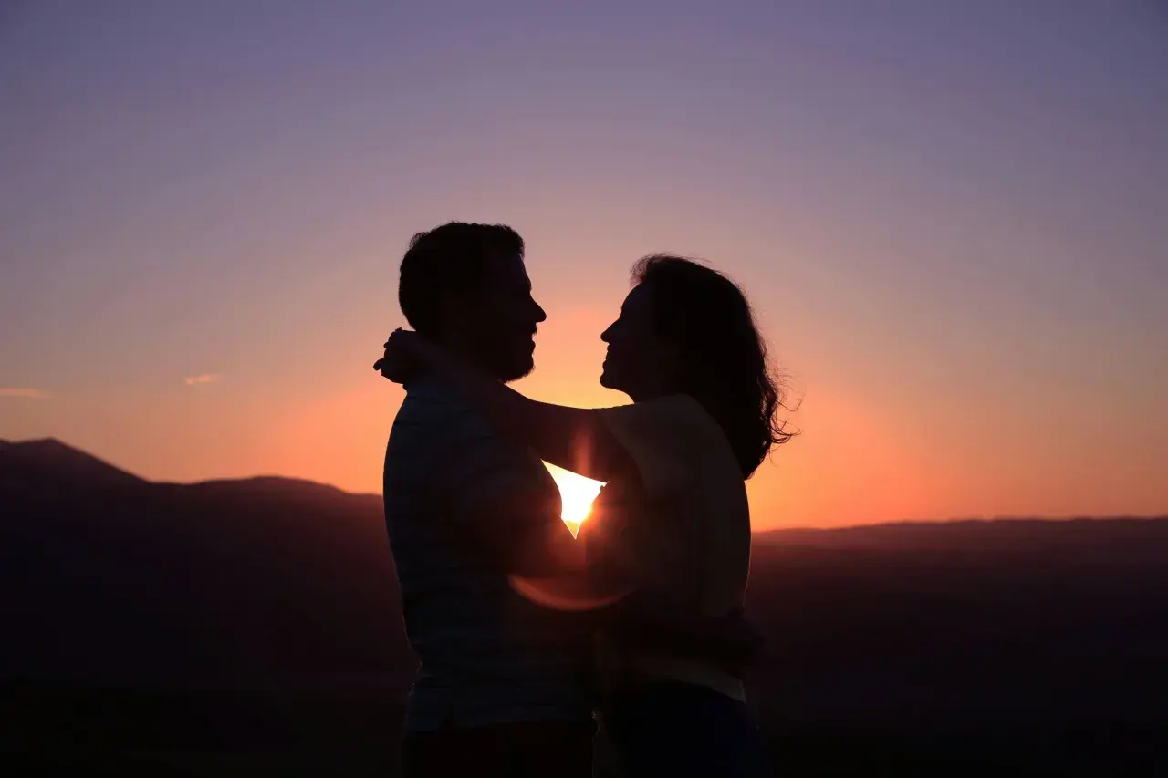 Siluetas de pareja abrazándose al atardecer. Su conexión irradia una profunda compatibilidad, como si fueran cáncer y cáncer, unidos por el amor.