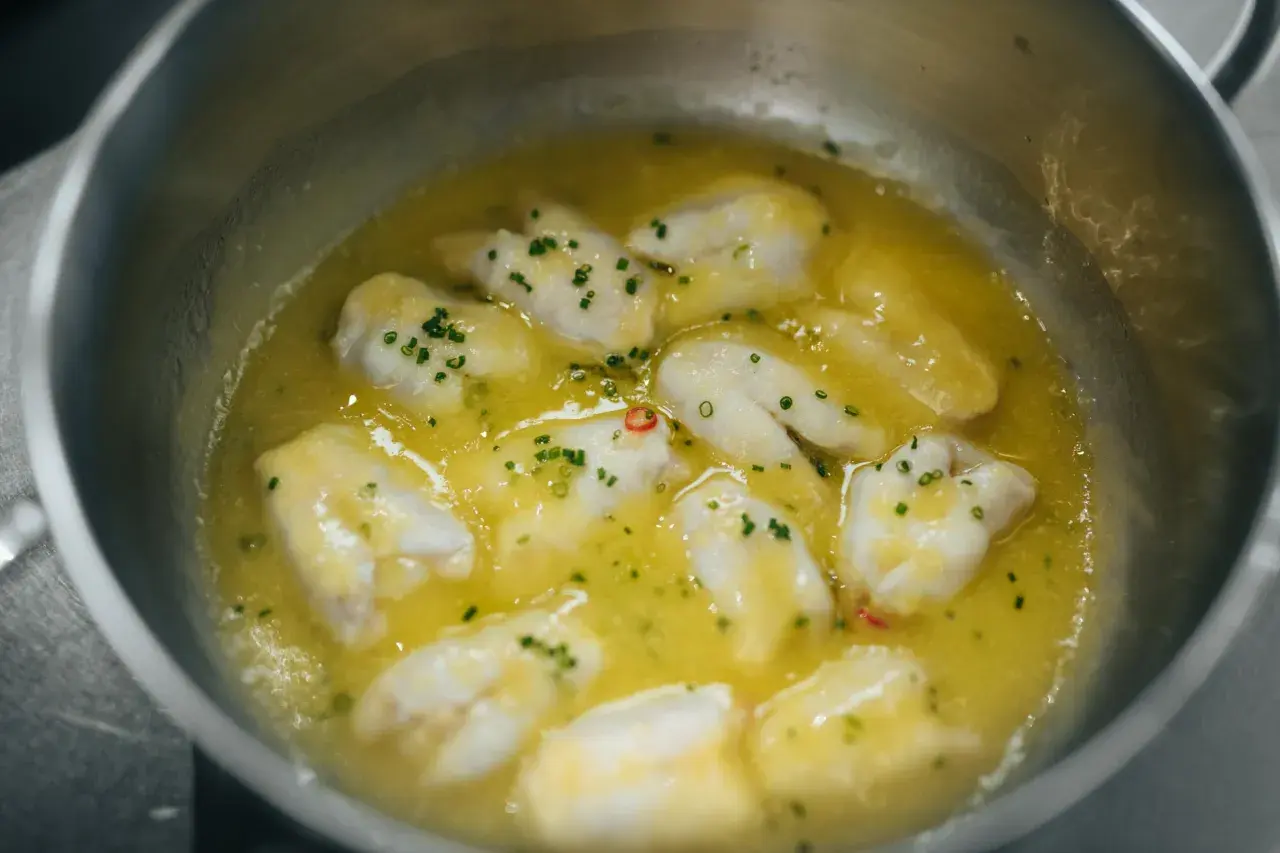 Trozos de bacalao cocinándose en aceite de oliva con ajo y guindilla, listos para la bacalao pil pil receta.