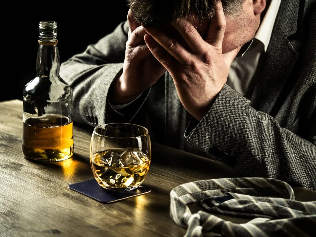 Hombre angustiado con botella y vaso de whisky. Busca remedios caseros para dejar de beber alcohol.