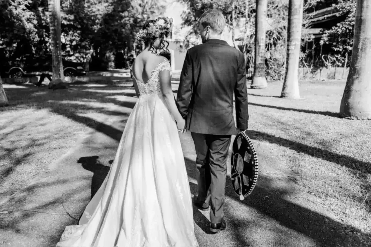 Novios caminando de la mano, ella con vestido de novia y él con traje y sombrero charro. Un recuerdo para todos los nombres de aniversarios de boda.