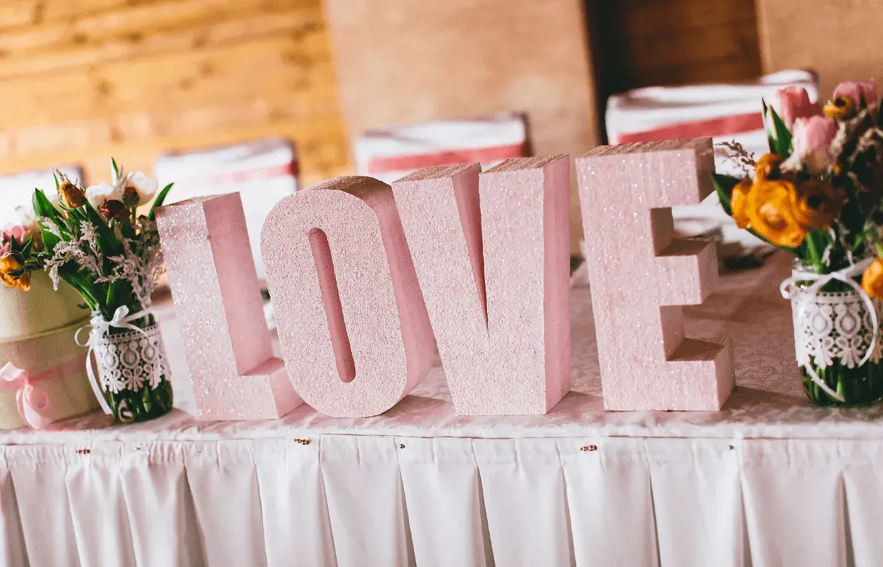 Letras gigantes "LOVE" en rosa brillante, un detalle perfecto para una decoración boda civil sencilla y barata. Flores a los lados.