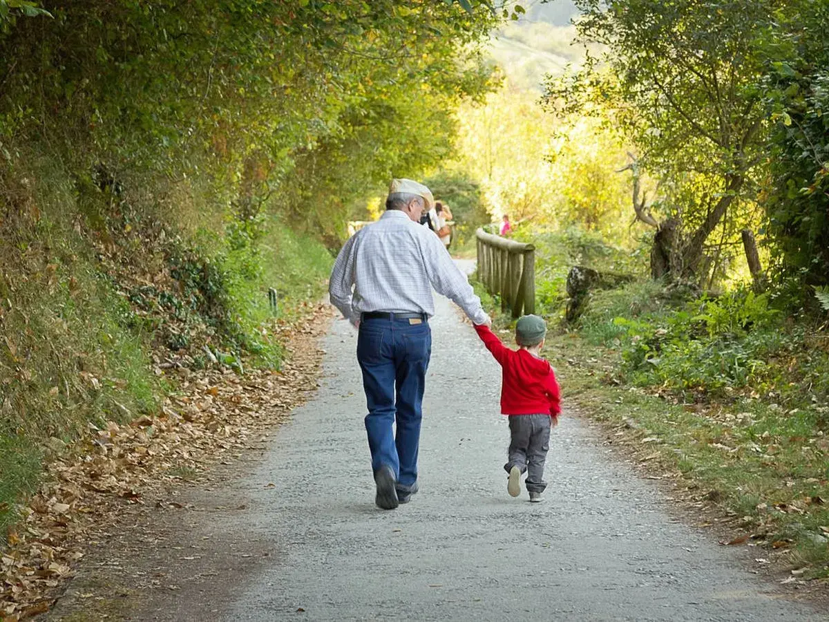 Abuelo y nieto caminan de la mano por un sendero otoñal. Un ejemplo de refranes cortos: "La unión hace la fuerza".