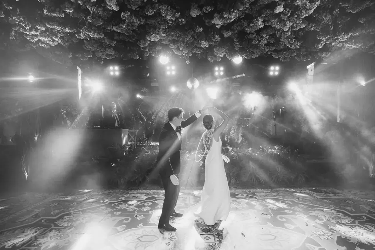 Novios bailando su primera canción, rodeados de luces y vegetación exuberante. La pista de baile decorada con un patrón intrincado.