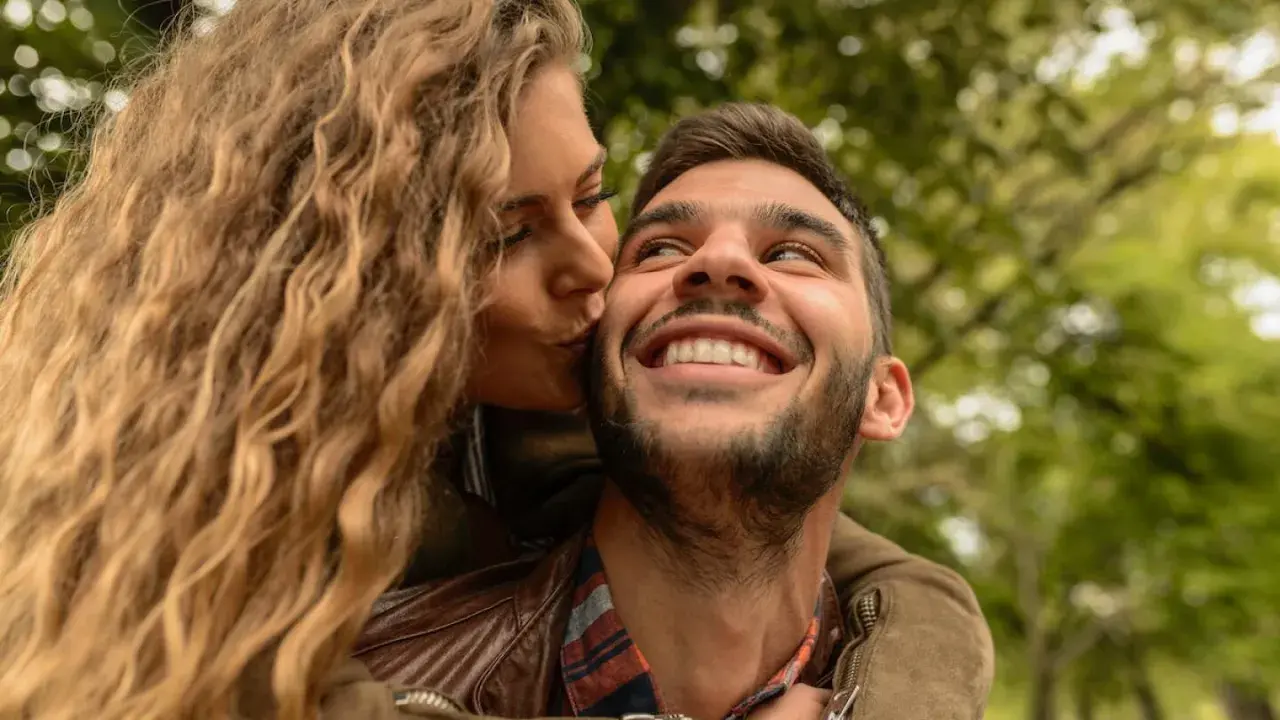 Una mujer rubia besa en la mejilla a un hombre sonriente. Las reglas de pareja se basan en el amor y la confianza.