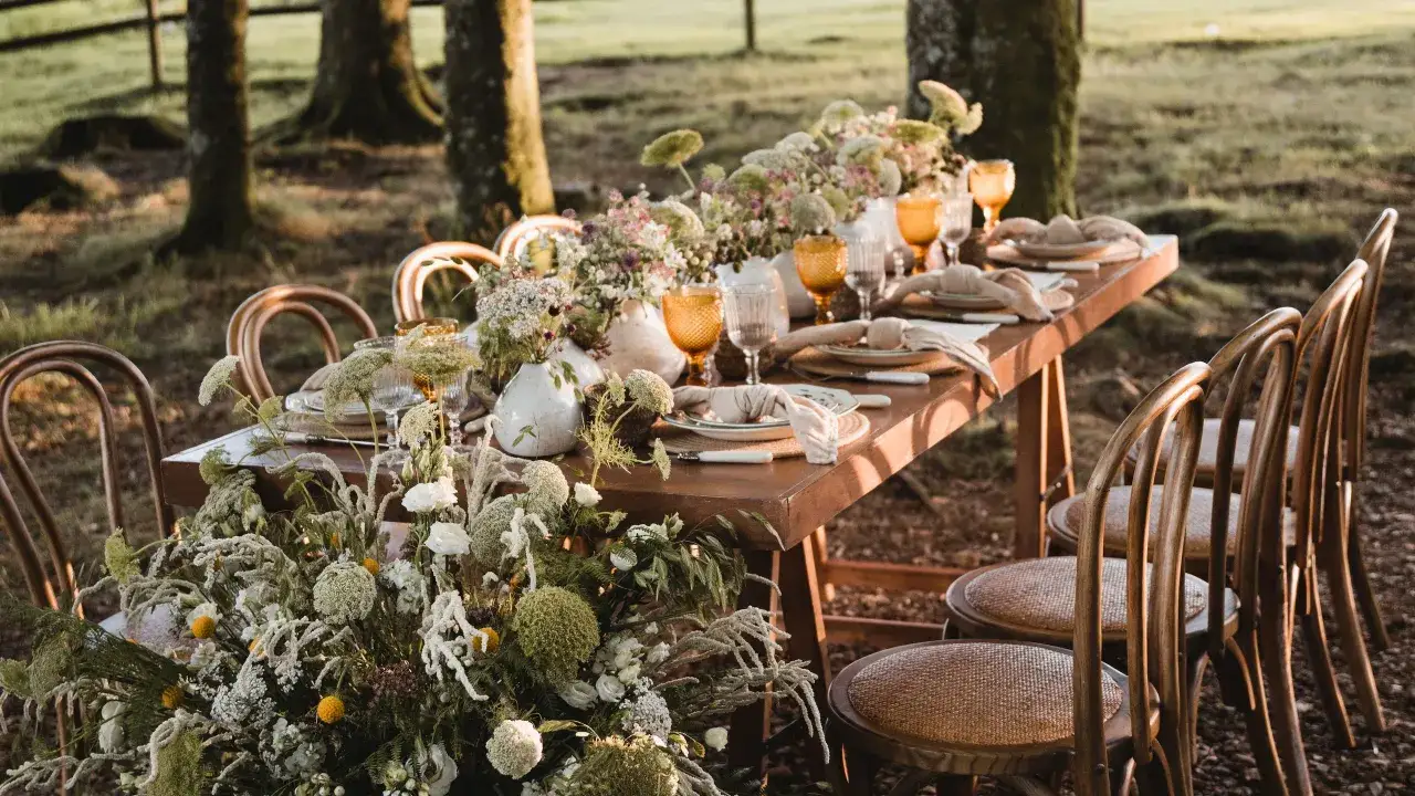Mesa de banquete al aire libre, decorada con flores silvestres y vajilla r&uacute;stica, lista para la boda del a&ntilde;o.