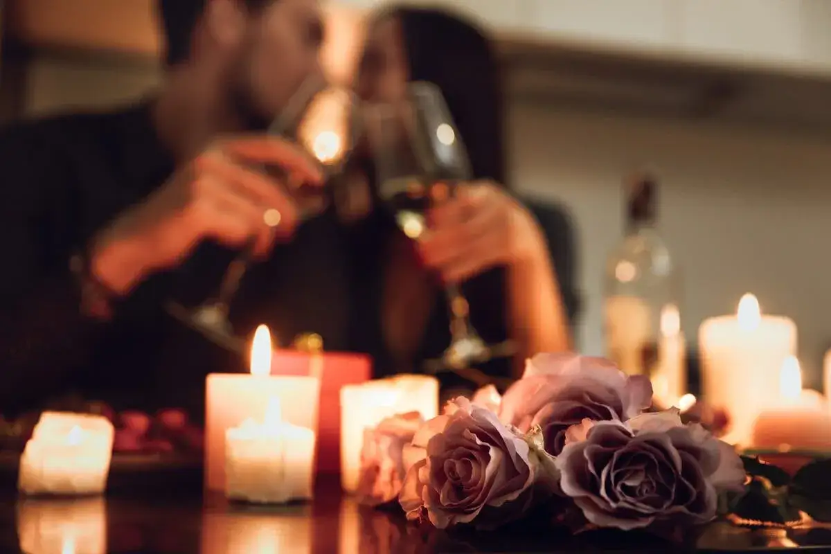 Pareja brindando en su aniversario 4 a&ntilde;os de casados, rodeados de velas y rosas.
