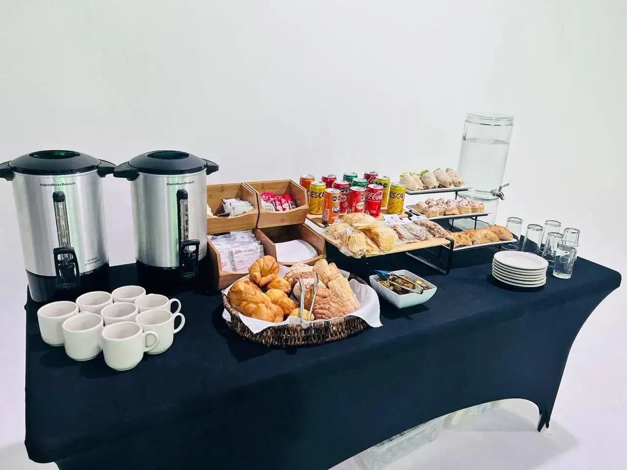 Montaje coffee break con dispensadores de café, tazas, bollería, sándwiches, patatas fritas y bebidas.