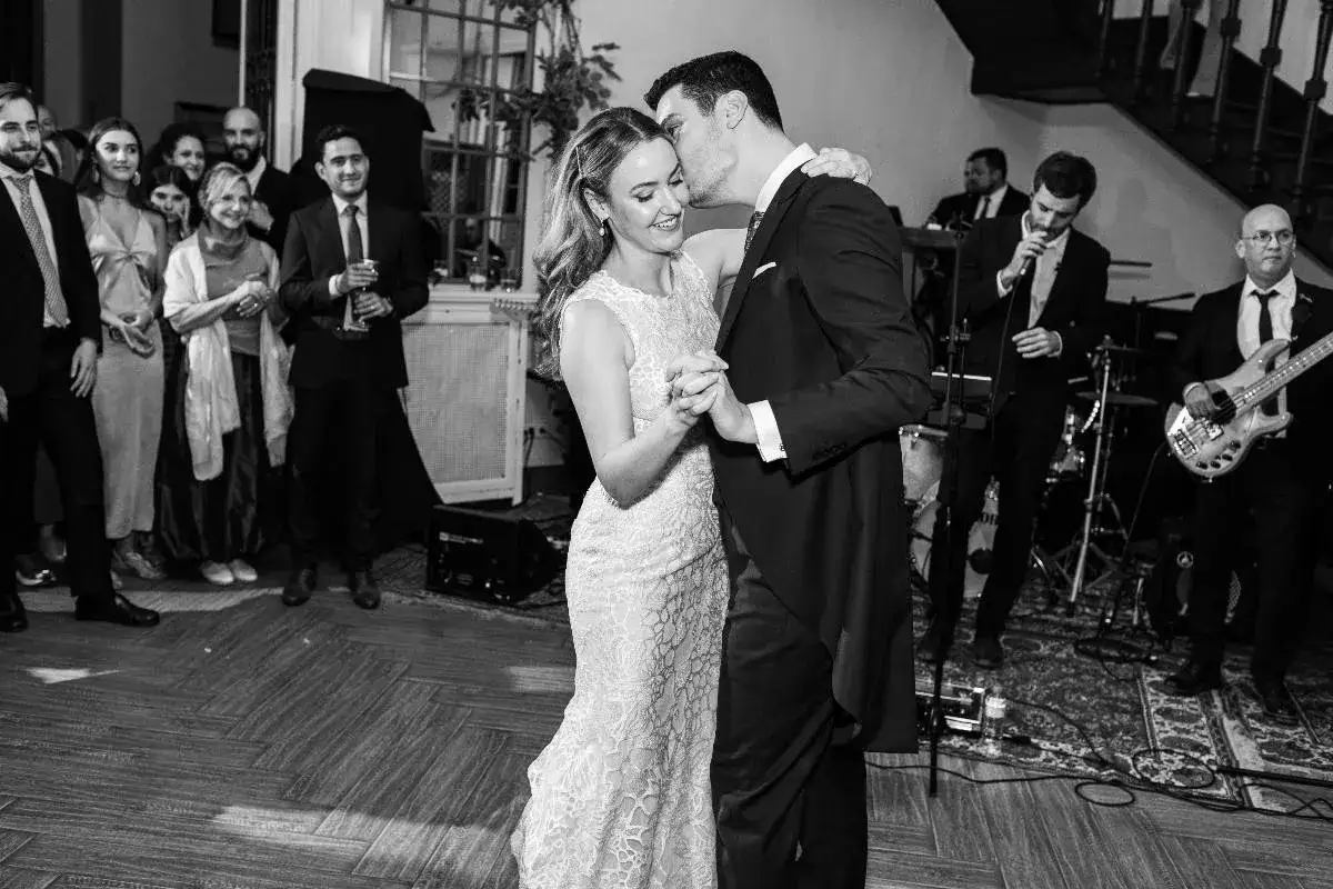 Novios bailando su vals de boda, rodeados de invitados y una banda musical.