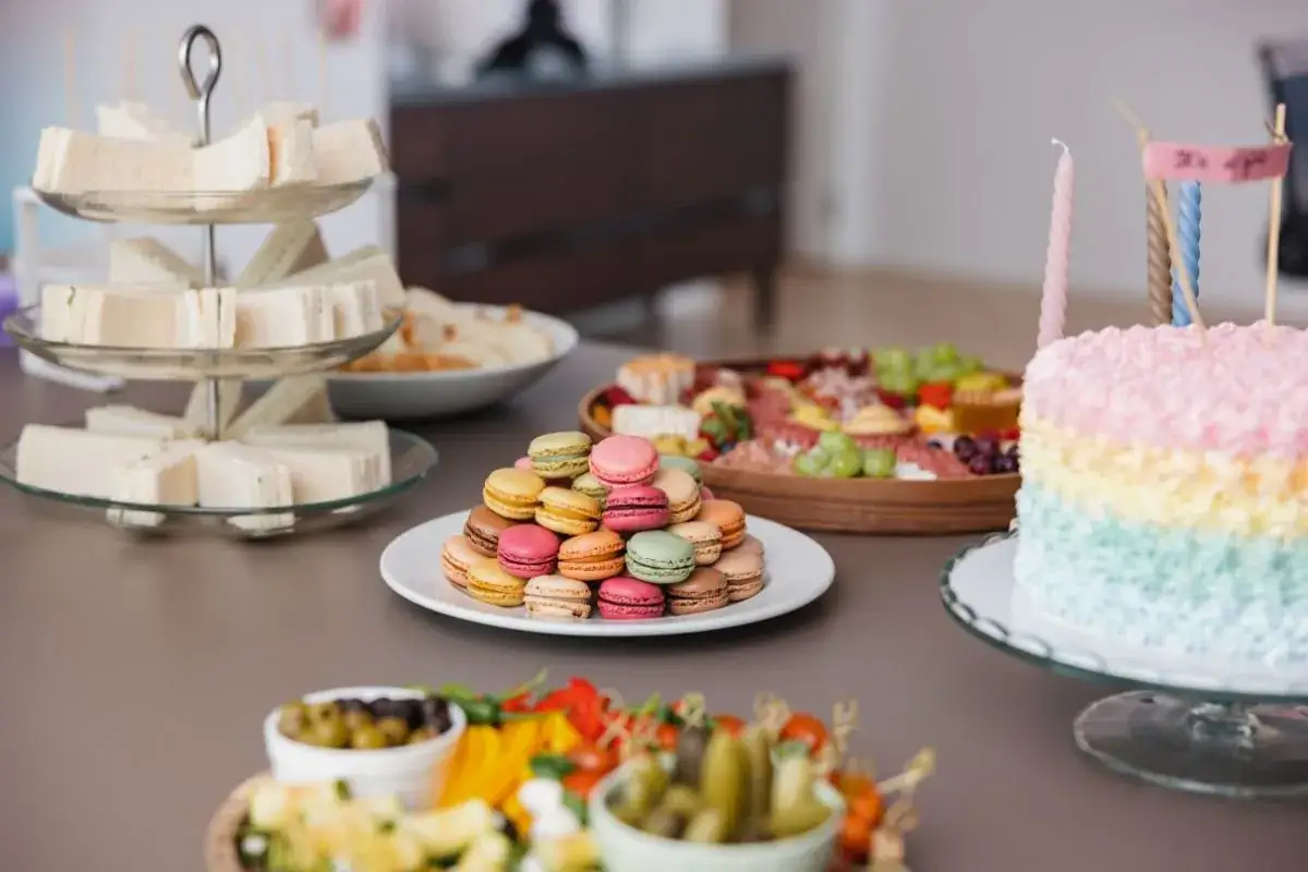 Mesa de baby shower con pastel de arcoíris, sándwiches, macarons y tabla de quesos. ¡Comida deliciosa para celebrar!