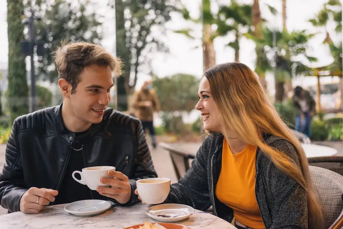 Una pareja joven comparte caf&eacute; y risas, un momento perfecto para aprender como enamorar a una mujer.