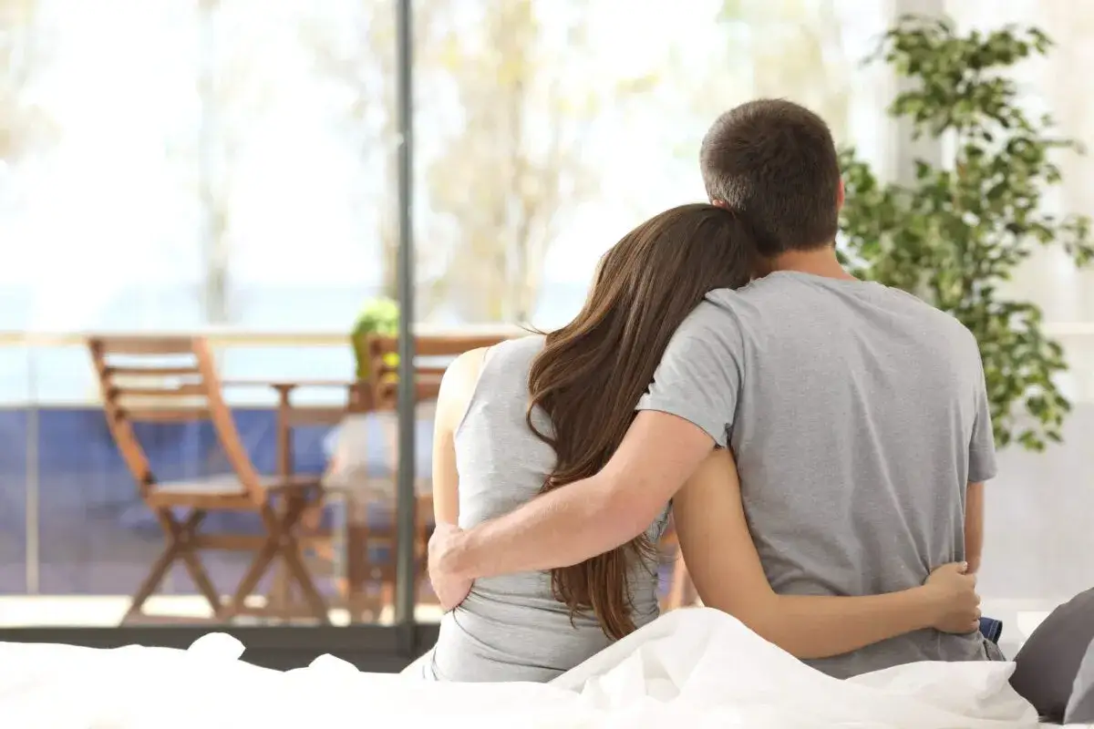 Pareja abrazada en la cama, mirando hacia afuera. Un momento de amor verdadero, paz y conexi&oacute;n.