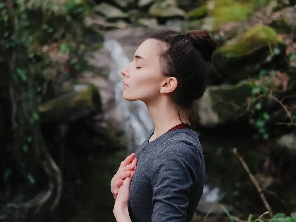 Mujer meditando en la naturaleza, un momento de paz para aprender como dejar de sobrepensar.