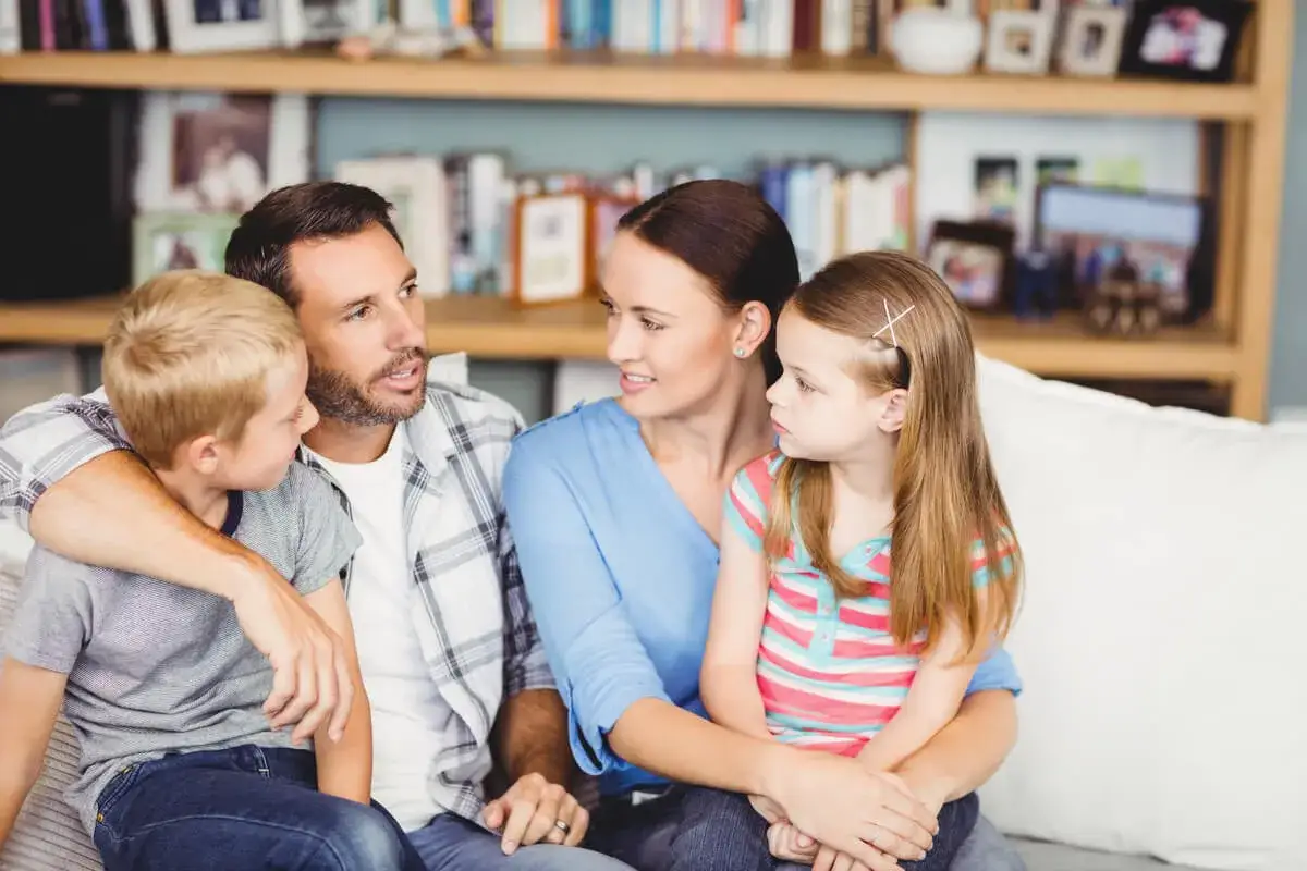 Familia reunida en el sof&aacute;, mostrando un ambiente de apego seguro. El padre abraza al hijo, mientras la madre mira a la hija.