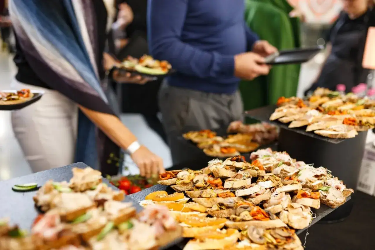 Un evento con servicio de catering, donde personas toman canap&eacute;s variados de una mesa de buffet.