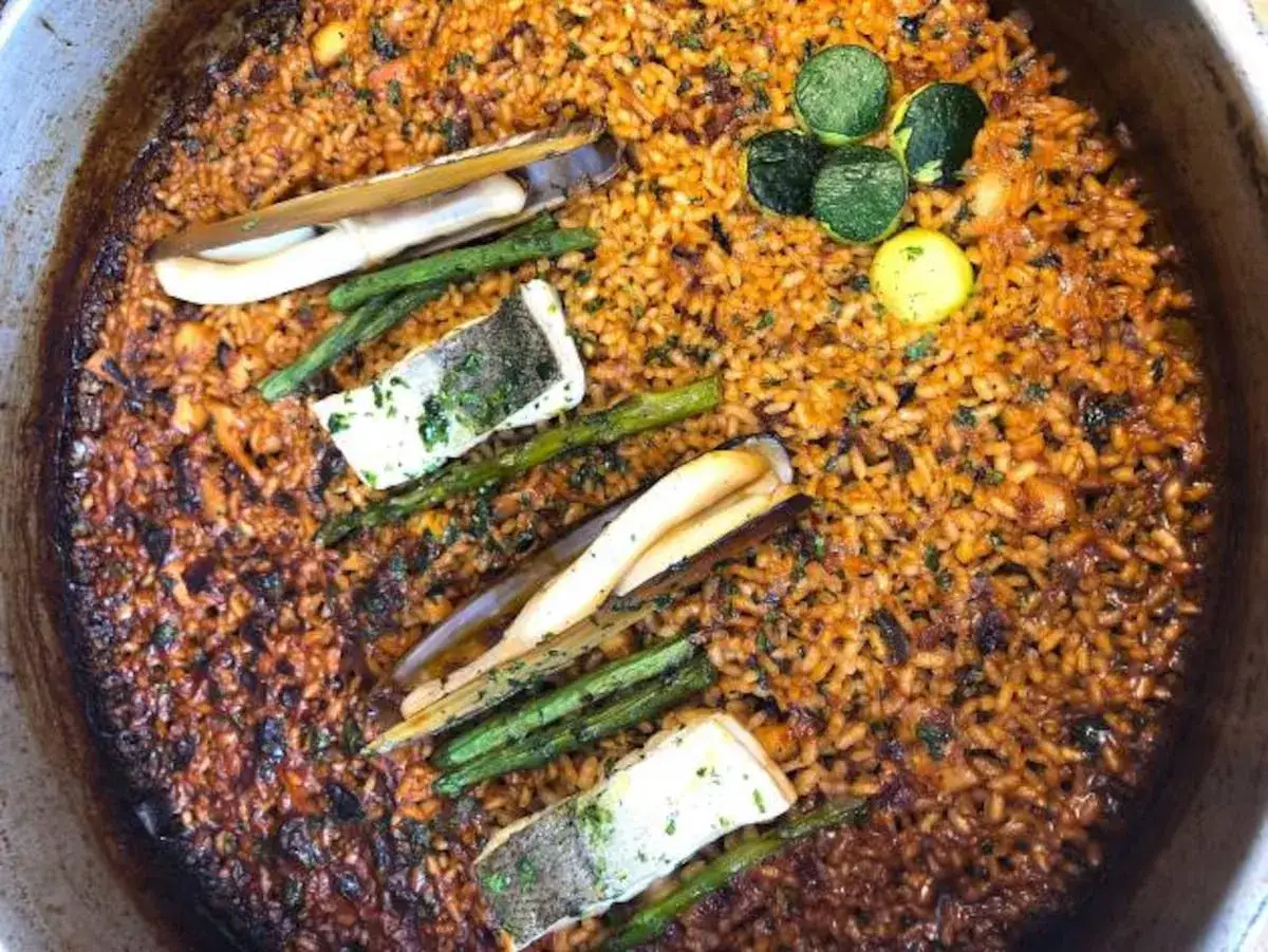 Paella de marisco con arroz pegado, esp&aacute;rragos, pescado y navajas.