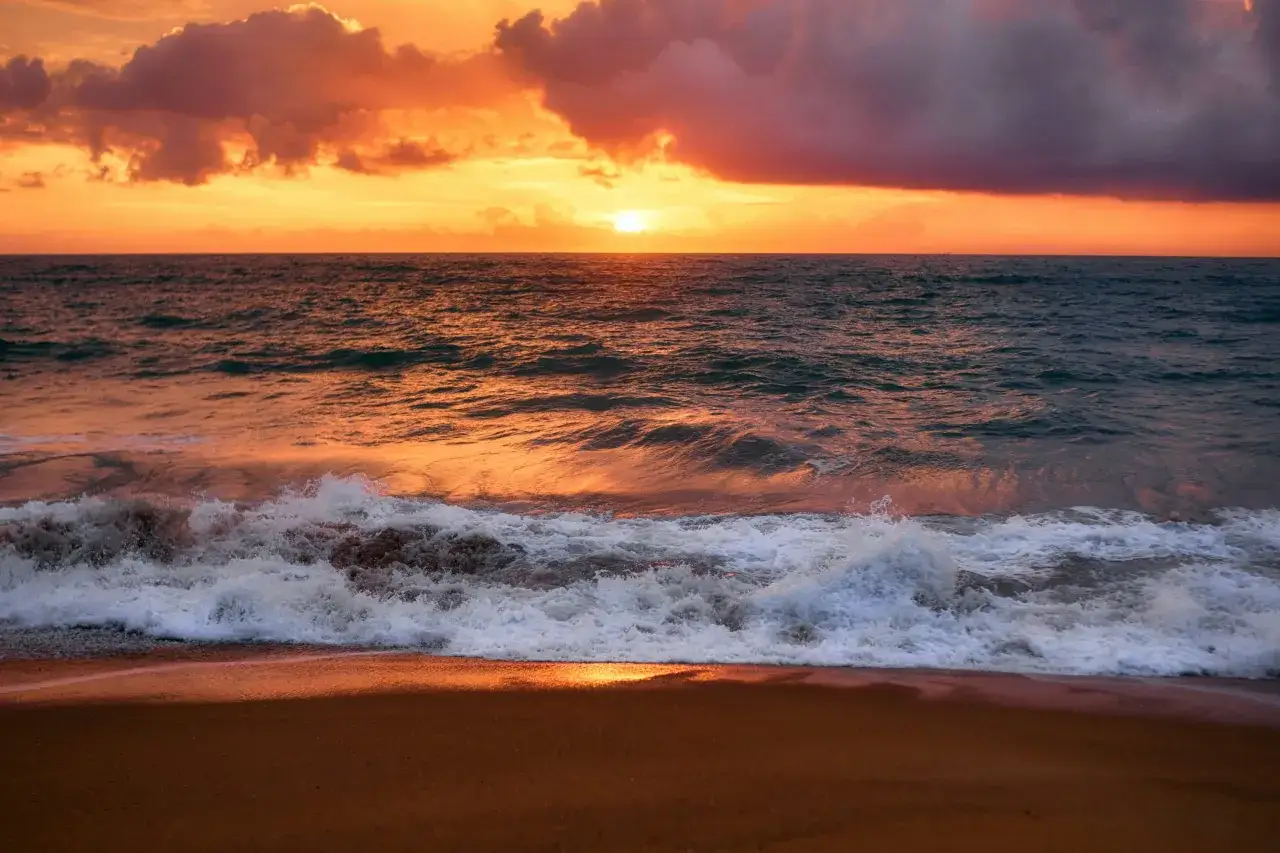 Olas rompiendo en la orilla bajo un cielo anaranjado, evocando frases sobre el mar y la calma.