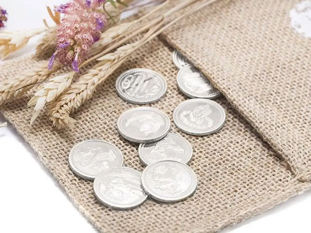Monedas plateadas, s&iacute;mbolo de prosperidad, junto a espigas y flores secas, representando las arras de boda.