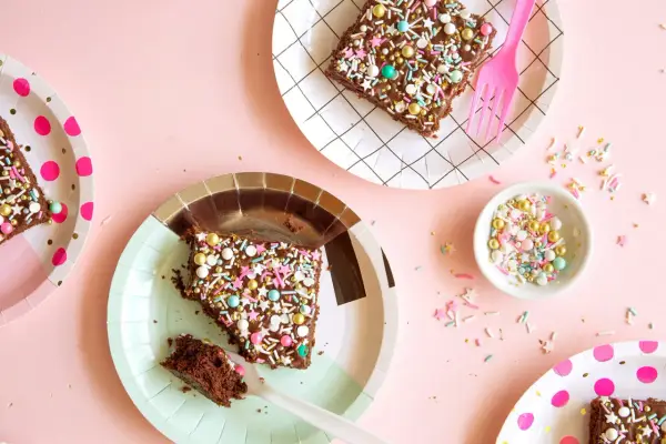 Deliciosos trozos de pastel de chocolate con chispas de colores y estrellas, listos para una merienda de cumpleaños infantil.