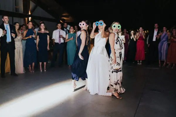 Un grupo de mujeres con gafas divertidas celebra una sorpresa para los novios en una fiesta.